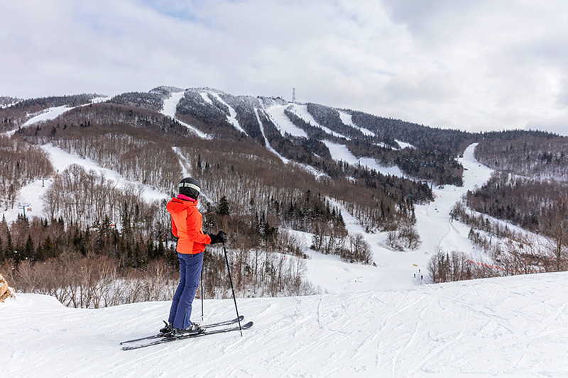 Woman in an orange jacket skiing and looking at the peak of Mont Tremblant.